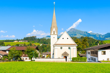 Fototapeta na wymiar Typical alpine church against Alps mountains background on green meadow in Reith bei Kitzbuhel village on sunny summer day, Tirol, Austria