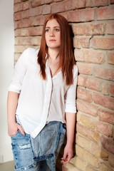 Daydreaming ginger girl leaning against brick wall