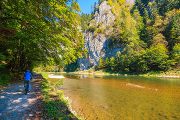 Woman cyclist riding along Dunajec river in autumn landscape of Pieniny Mountains, Poland