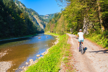 Young woman cycling along Dunajec river on sunny autumn day, Pieniny Mountains, Poland