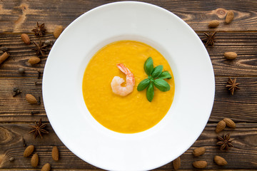 Tasty pumpkin cream soup with shrimps and basil leaves, blended with spice and carrots. Top view.