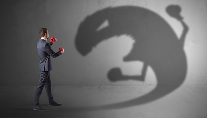Businessman with boxing glove fighting with a big monster shadow
