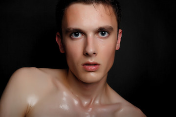 Handsome young man isolated. Beauty portrait of shirtless muscular man is standing on black background and looking at camera. Men's health.
