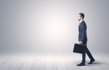 Successful businessman walking in front of an empty wall with briefcase on his hand
