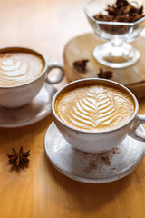 two cups of cappuccino with a beautiful pattern on milk foam. Wooden table with space for text. The view from the top.