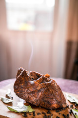 Baked beef shank with spices, close-up on the table, a hot dish with smoke from the oven