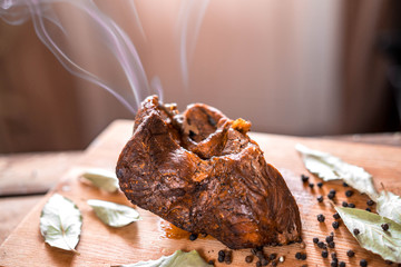 Baked beef shank with spices, close-up on the table, a hot dish with smoke from the oven