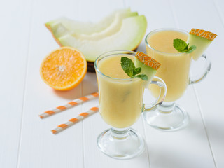 Two glass mugs with pieces of melon and mint on a white wooden table.