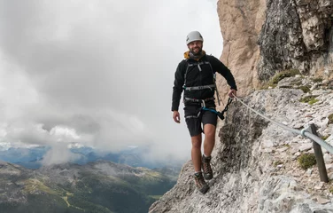 Foto auf Acrylglas young male mountain climber on a steep and exposed Via Ferrata in Alta Badia in the South Tyrol in the Italian Dolomites © makasana photo