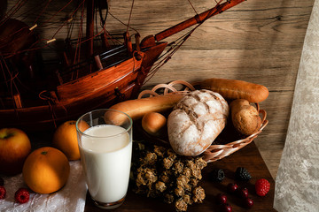 still life of breakfast set of milk variety kinds of bread in basket and fruits on wooden table near lace curtain by window