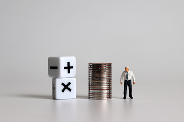Miniature man standing with a cube with a mathematical symbol and a pile of coins.