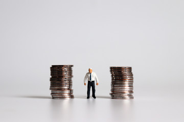 A miniature old man standing among a pile of coins.