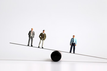 Miniature men standing on the seesaw.