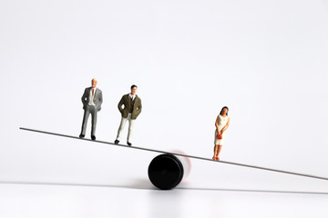 Two miniature men and a miniature woman standing on the seesaw.