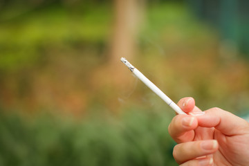 Female hand with smoking cigarette on blurred green park background