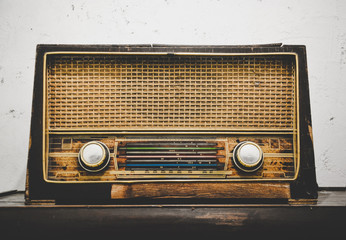 old retro wooden radio reciever on wooden table with white grunge cement plaster wall background, vintage effect