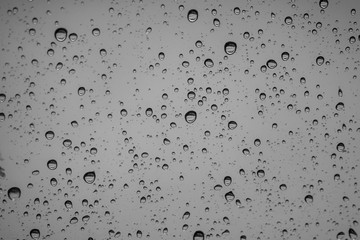 Rain drops on outside car mirror window glasses surface with cloudy background . Natural pattern of raindrops on cloudy background. Shallow depth of field.
