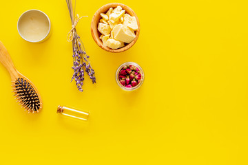 Hair treatment with natural products. Jojoba, argan, coconut oil near bunch of lavender and hairbrush on yellow background top view copy space