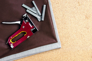 Stapler and staples on the fabric, on chipboard. Top view from an angle.