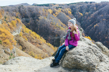Naklejka premium girl in purple jacket and gray hat sits on top of mountain and smiles