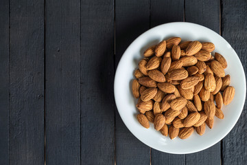 Top view of almonds on a white dish on black wooden table.
