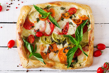 Mozzarella, tomatoes, basil savory pie on a white wooden background. Delicious food, appetizer in a mediterranean style. Top view. Flat lay