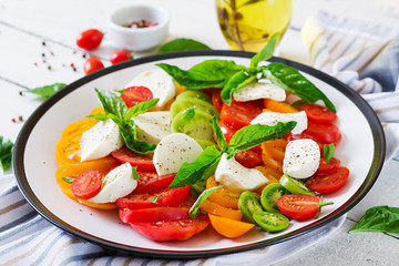 Mozzarella cheese, tomatoes and basil herb leaves in plate on the white wooden table. Caprese salad. Italian food.