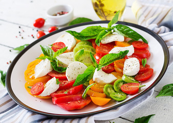 Mozzarella cheese, tomatoes and basil herb leaves in plate on the white wooden table. Caprese salad. Italian food.