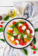 Mozzarella cheese, tomatoes and basil herb leaves in plate on the white wooden table. Caprese salad. Italian food. Top view