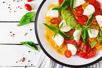 Mozzarella cheese, tomatoes and basil herb leaves in plate on the white wooden table. Caprese salad. Italian food. Top view