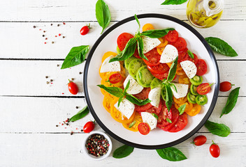 Mozzarella cheese, tomatoes and basil herb leaves in plate on the white wooden table. Caprese salad. Italian food. Top view