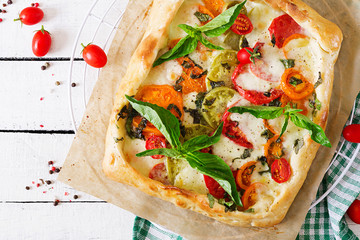 Mozzarella, tomatoes, basil savory pie on a white wooden background. Delicious food, appetizer in a mediterranean style. Top view. Flat lay