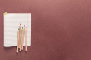 Top view over a school supplies as pencils, work book and paper clip from left side of a brown background. Back to school concept. Office supplies flat lay