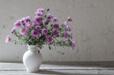 violet flowers in white vase on old background