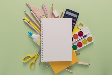Opened blank notebook over the school supplies such as scissors, rulers, magnificent glass, tapes, calculator, pins, paper clips and paints. Back to school and education concept.