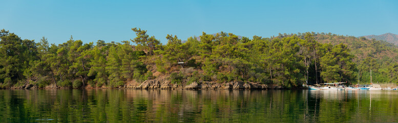 Panoramic view from a bay in Mediterranean with pine trees and the reflection on sea and boats