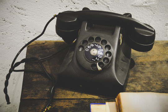 black vintage telephone on wooden table with old blank notebook and white grunge cement plaster wall, vintage effect