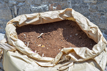 Opened big plastic bag full of soil standing niea the stone wall.