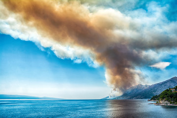 Dangerous dark red smoke and dust over the sea. Burning mountain forest in fire . Adriatic Coast in Croatia. Dramatic climate disaster landscape