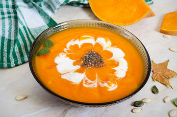 Delicate pumpkin puree with cream and chia seeds in a black glass bowl on a light background.