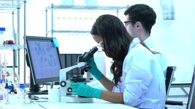 Scientist is looking through microscope with colleagues working in modern laboratory or medical center. Concept of science, testing development and lab industry.