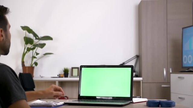 Man at his desk in front of computer with green screen. Mock up video for your data. Dolly slider 4K footage