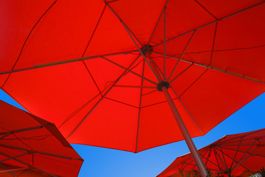 Close up of three red cafe umbrellas filling the frame and blue sky between them. Patio umbrellas as seen from bottom
