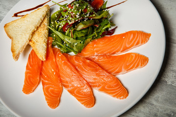 closeup salmon slices served with rucola and tomato salad and toasted bread