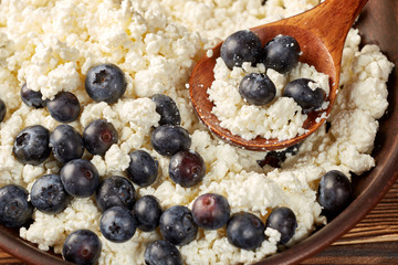 Cottage cheese with ripe blueberries in a clay bowl with a wooden spoon.