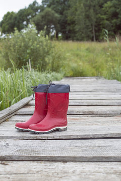 Red rubber boots stand on the old wooden bridge, background