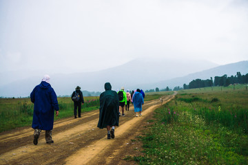 People go forward in mountain despite bad weather. Travelers goes upwards along road after dog. Way on foot in highlands in rainy overcast day. Summit despite everything. Walking in mountains.
