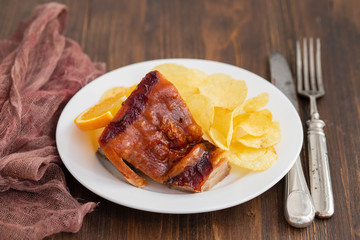 roasted piglet with potato chips and orange on white plate