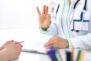Doctor showing Ok sign to patient while sitting at the desk in hospital office, closeup of human hands. Medicine and health care concept