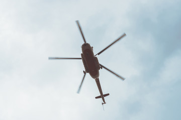 Fototapeta na wymiar Silhouette of big helicopter overhead on background of overcast blue sky in faded tones. Aerial tourism. Rescue mission. Air ambulance. Emergency evacuation.